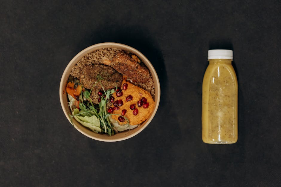 A vibrant vegan bowl with quinoa, fresh vegetables, and a smoothie bottle against a dark backdrop.